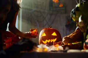 Close up of Jack O' Lantern on dining table with unrecognizable people arranging it on Halloween.